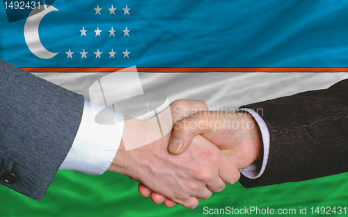 Image of businessmen handshake after good deal in front of uzbekistan fla