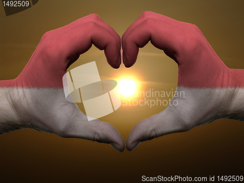 Image of Heart and love gesture by hands colored in indonesia flag during