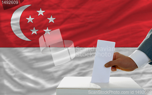 Image of man voting on elections in singaporel in front of flag