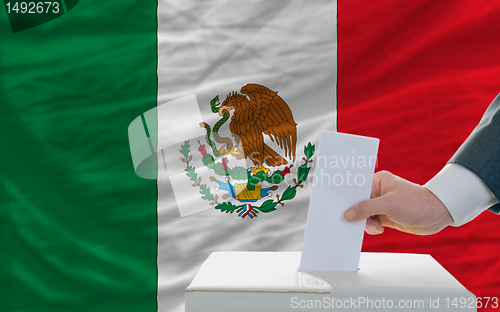 Image of man voting on elections in mexico in front of flag