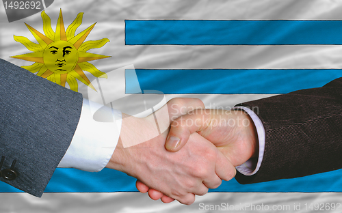 Image of businessmen handshake after good deal in front of uruguay flag