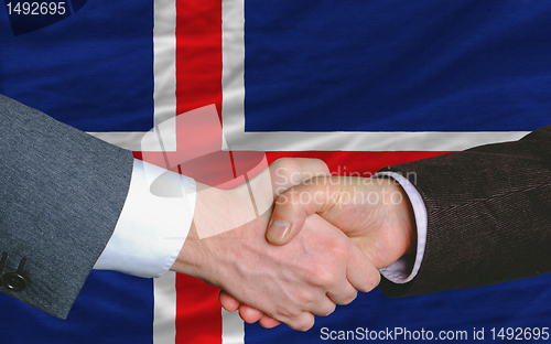 Image of businessmen handshake after good deal in front of iceland flag