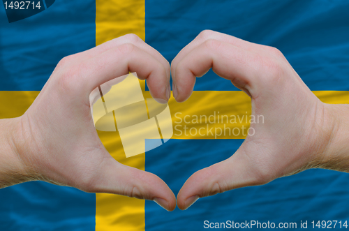 Image of Heart and love gesture showed by hands over flag of sweden backg