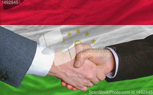 Image of businessmen handshake after good deal in front of tajikistan fla