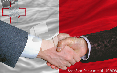 Image of businessmen handshake after good deal in front of malta flag