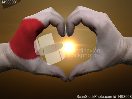 Image of Heart and love gesture by hands colored in japan flag during bea