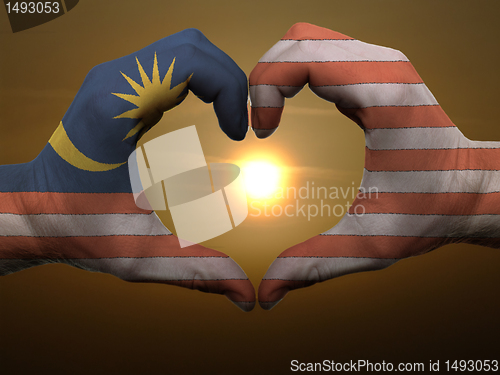 Image of Heart and love gesture by hands colored in malaysia flag during 