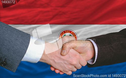 Image of businessmen handshake after good deal in front of paraguay flag