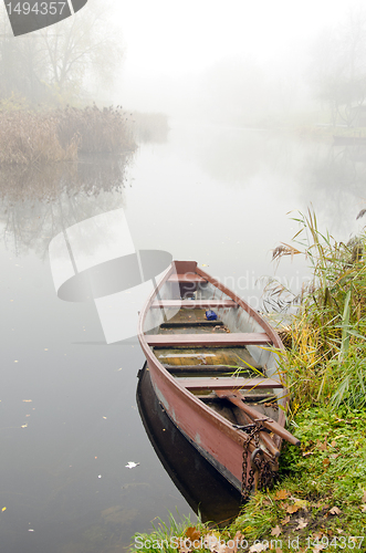 Image of Wooden boat on coast of river sunken in dense fog.