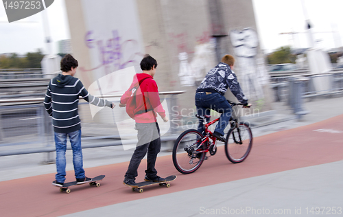 Image of Teenagers ride bike and skateboard. Bicycle trail.