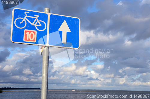 Image of Bicycle path sign nr ten near lake and cloudy sky.