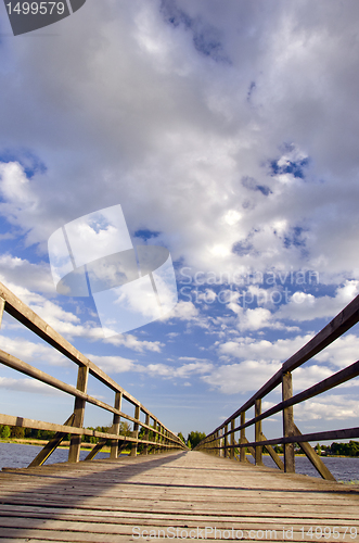 Image of Long wooden plank bridge over lake and cloudy sky.