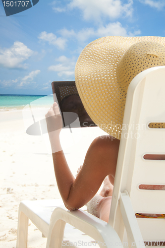 Image of Woman sitting on the beach and browsing internet with tablet computer