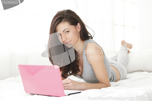 Image of young girl looking at the camera while in bed with computer