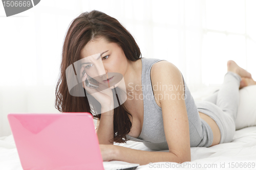 Image of Girl worried while using phone and computer  in bed