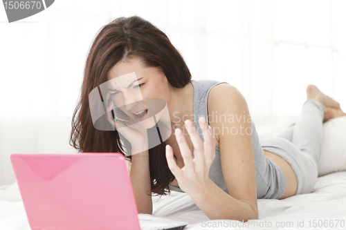 Image of Girl screaming on the mobile phone with computer in bed