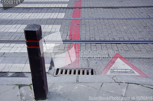 Image of Sidewalk and tram rails. Warning sign street.