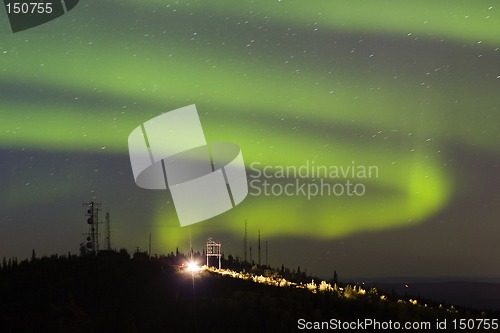 Image of Aurora Borealis over hill with antennas and car with lights on