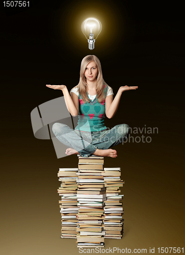 Image of woman in lotus pose balancing on pile of books and bulb