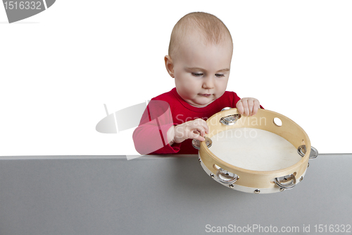 Image of young child holding tambourine behind grey shield