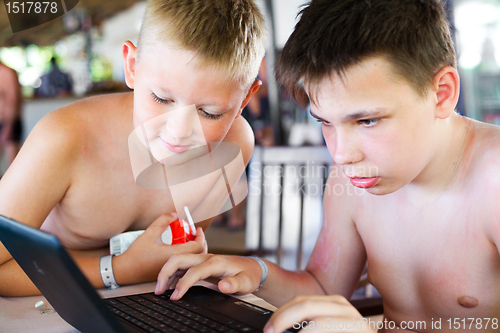 Image of Two boys play a laptop on rest in a bar on a beach