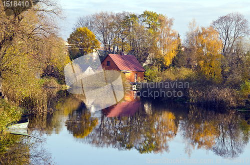 Image of Village houses near river. Autumn trees water boat