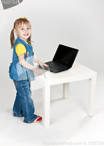 Image of little girl in blue jeans standing at a table with a laptop