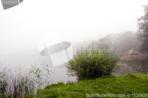 Image of Mystic lake fog green coastal flora and small hut 