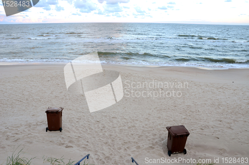 Image of Garbage containers sea sand waves backdrop 