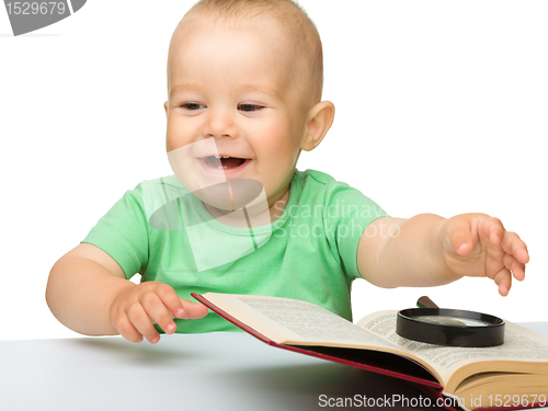 Image of Little child play with book and magnifier