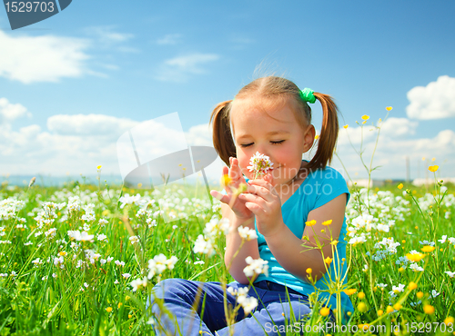 Image of Little girl is smelling flowers on green meadow