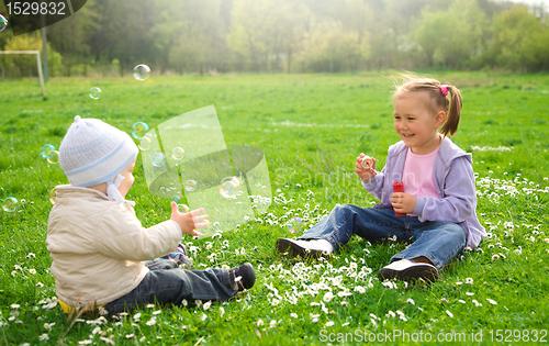 Image of Two children are sitting on green meadow