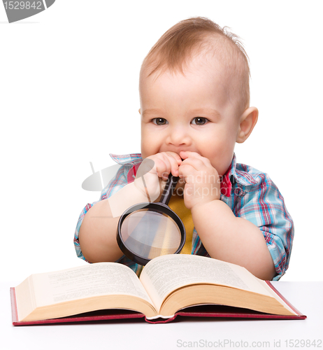 Image of Little child play with book and magnifier