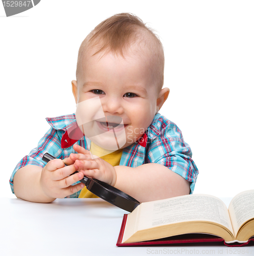 Image of Little child play with book and magnifier