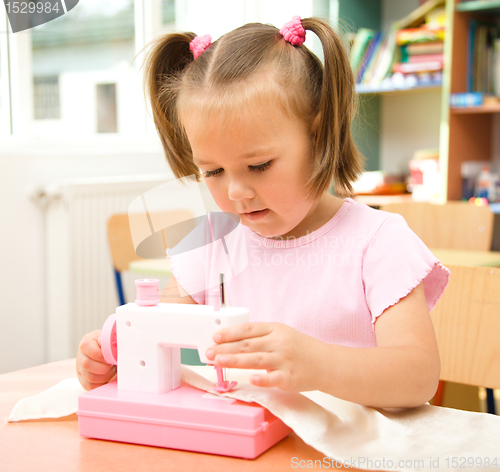 Image of Little girl is playing with sewing machine