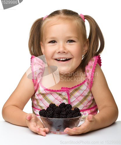 Image of Cheerful little girl is eating blackberry