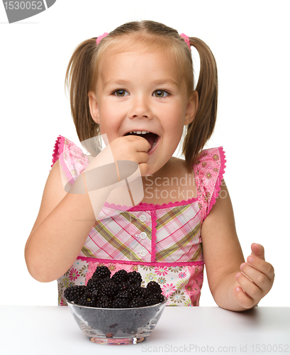 Image of Cheerful little girl is eating blackberry