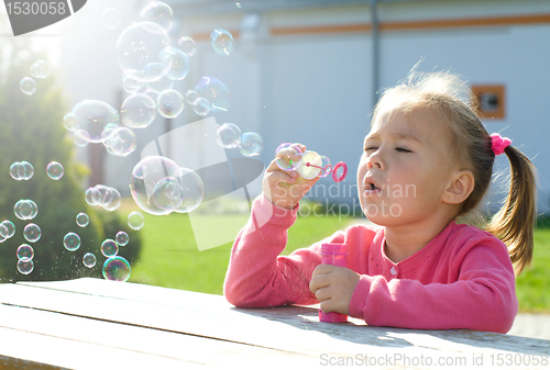 Image of Little girl is blowing soap bubbles