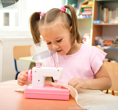 Image of Little girl is playing with sewing machine