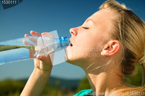 Image of Young woman is drinking water outdoors