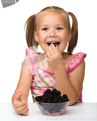 Image of Cheerful little girl is eating blackberry