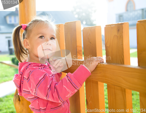 Image of Cute little girl is standing near a fence