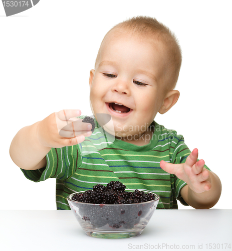 Image of Cheerful little boy is eating blackberry
