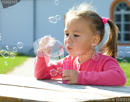 Image of Little girl is blowing soap bubbles
