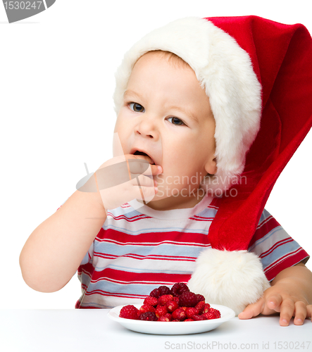 Image of Cute little boy eating berries wearing santa hat
