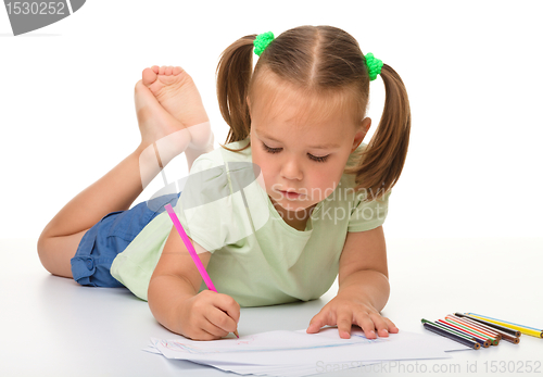 Image of Little girl is drawing while laying on the floor