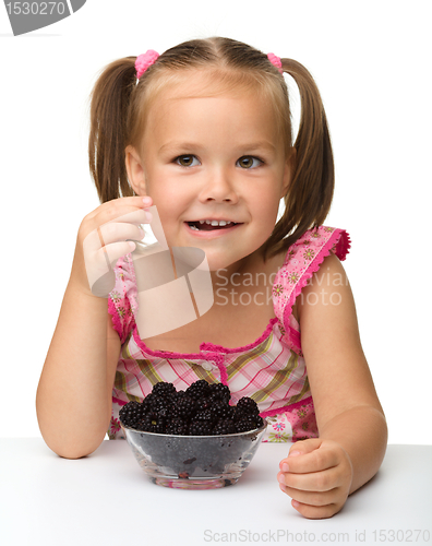 Image of Cheerful little girl is eating blackberry