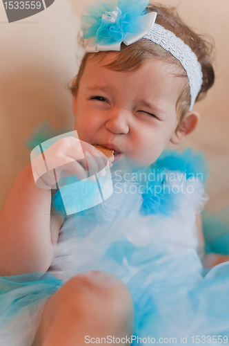 Image of Little girl in the blue dress eats cookie