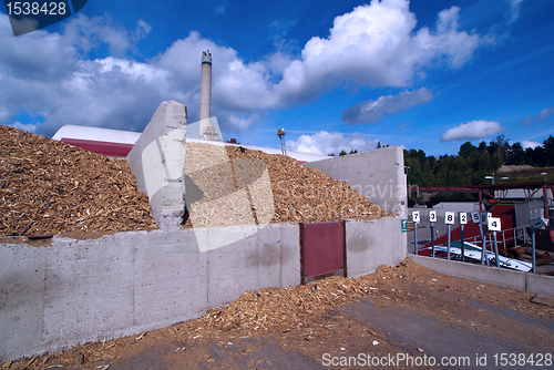 Image of bio power plant with storage of wooden fuel against blue sky