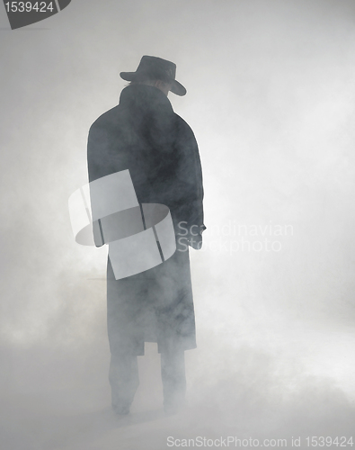 Image of Woman wearing trench coat and standing in fog